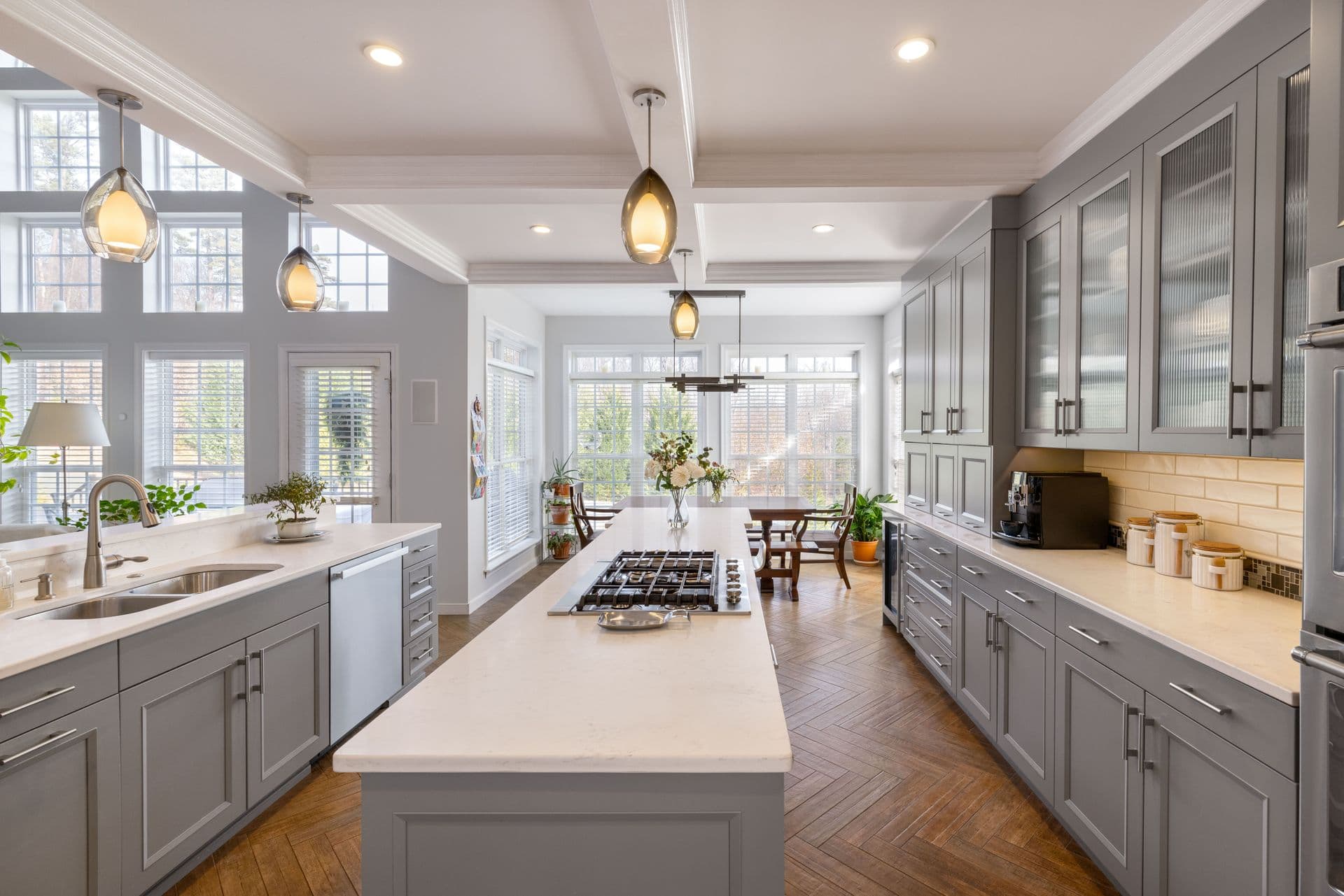 Bright modern kitchen with gray cabinetry, white quartz countertops, center island with gas cooktop, pendant lighting, and large windows overlooking outdoor landscape